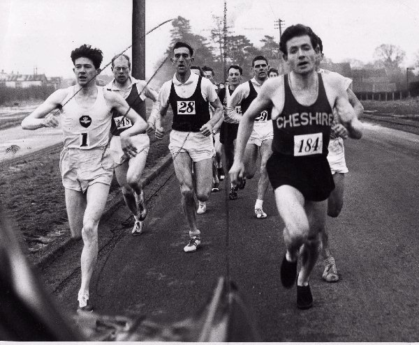 Brian Craig and Ron Barlow jostle for first position soon after the start of the St. Asaph to Rhyl road race organized annually by the Rhyl Athletic Club. Craig number 1 is from Blackpool and Barlow number 184 is from Wallasey A.C.