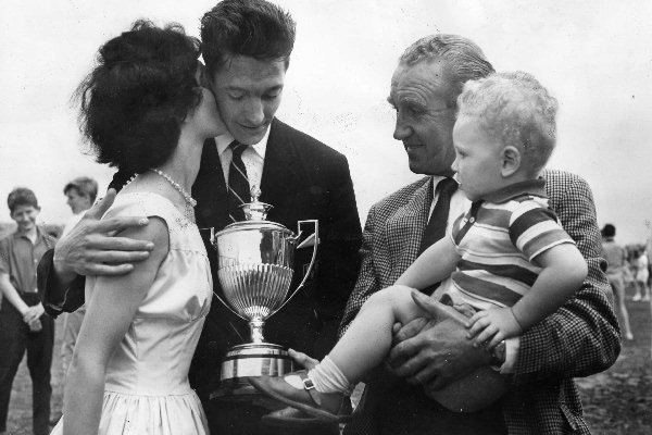 Mr Ernest Marples, Minister of Transport and M.P. for Wallasey is left holding baby (two year old Geoffrey Mather) as twenty-five-year-old Kevin Mather of Wallasey congratulatory from his wife Anne after winning the Marples Trophy for being Wallasey's Sports Personality of the Year 1962.